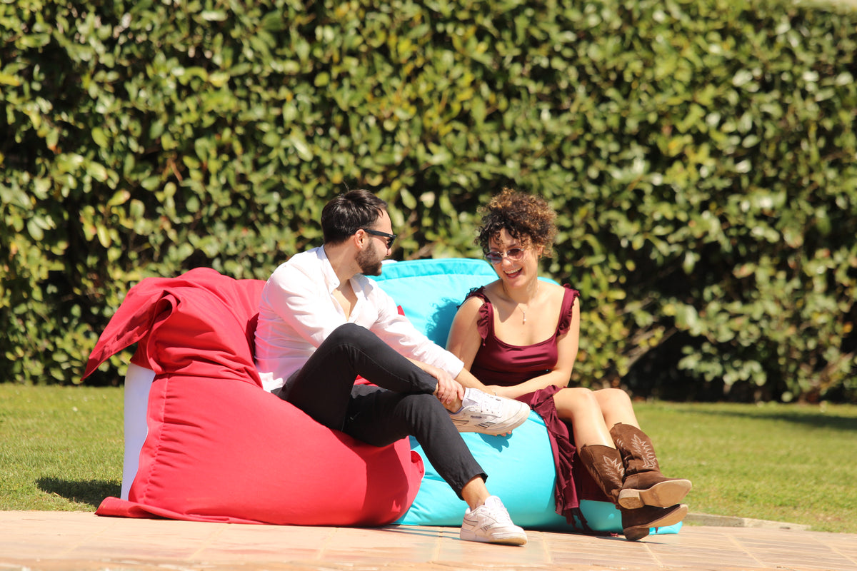 Due persone sedute su pouf Belly rosso e turchese accanto alla piscina
